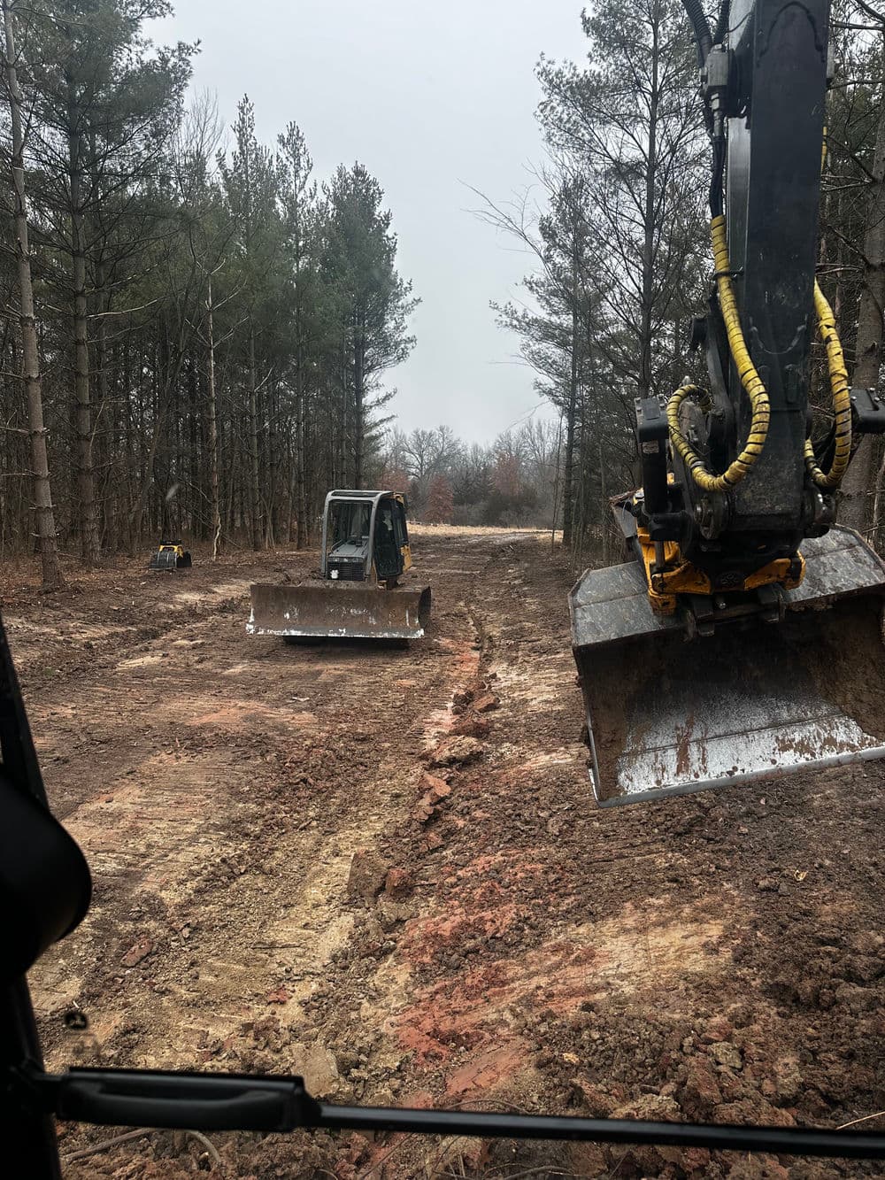 Excavator operating on cleared land surrounded by trees for construction project.