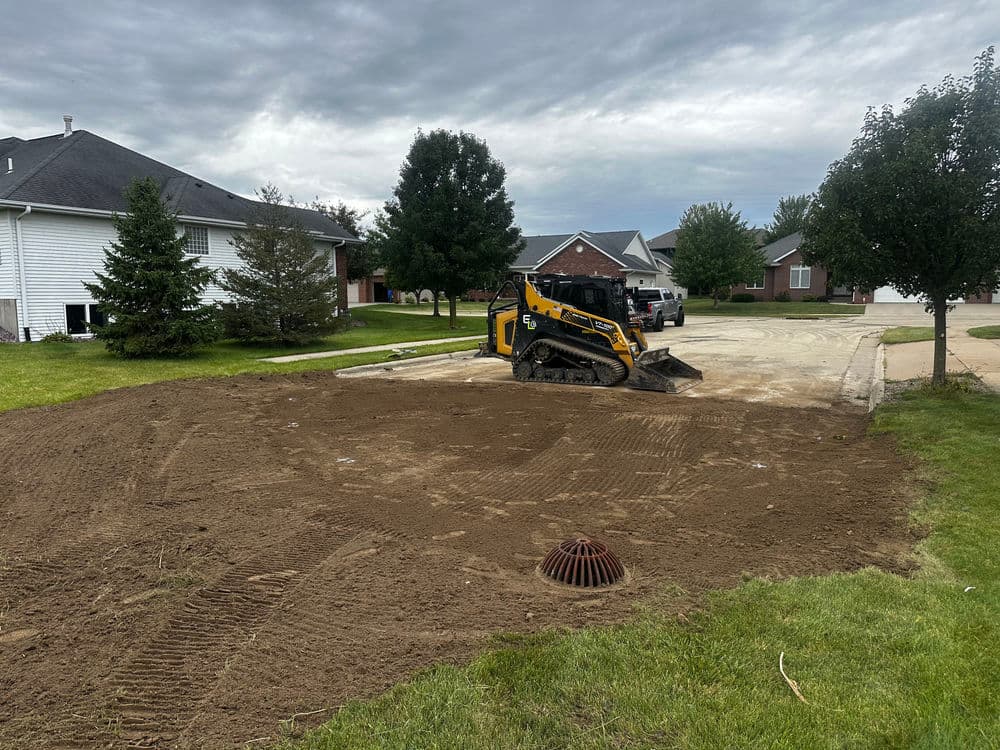 Skid steer loader on residential lot preparing land with cloudy sky overhead.
