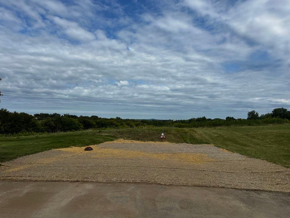 Open landscape with a flat, gravel area and scattered hay under a cloudy sky.