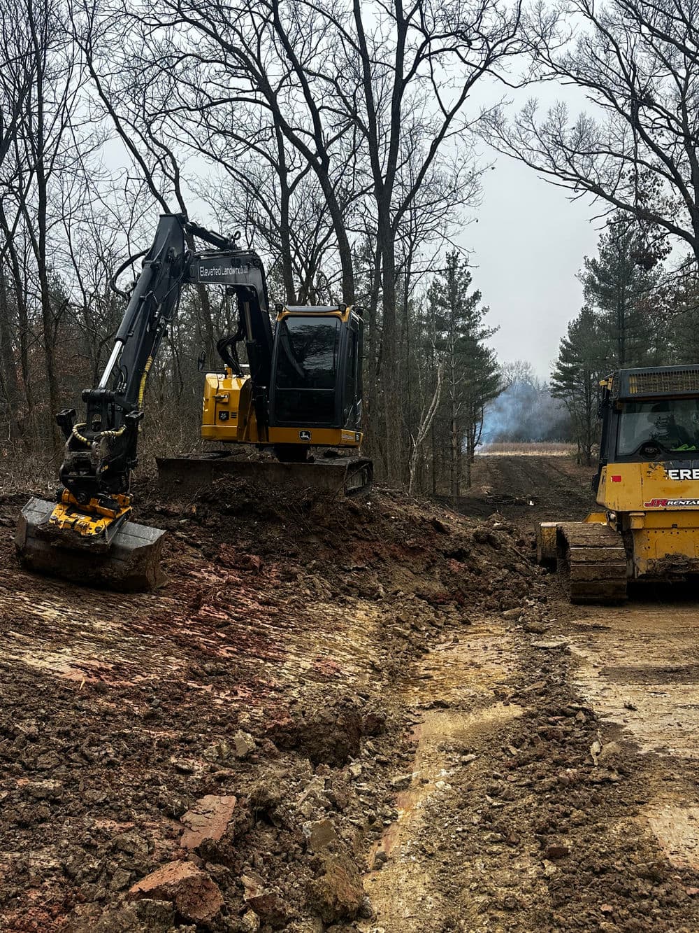 Excavator and bulldozer clearing land in forested area for construction project.