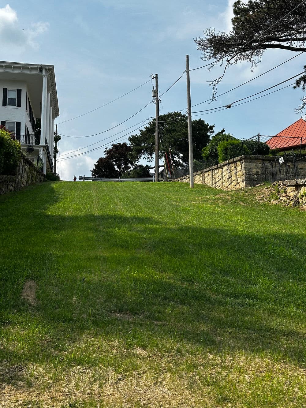 Lush green hillside leading up to a white building with utility poles and trees.