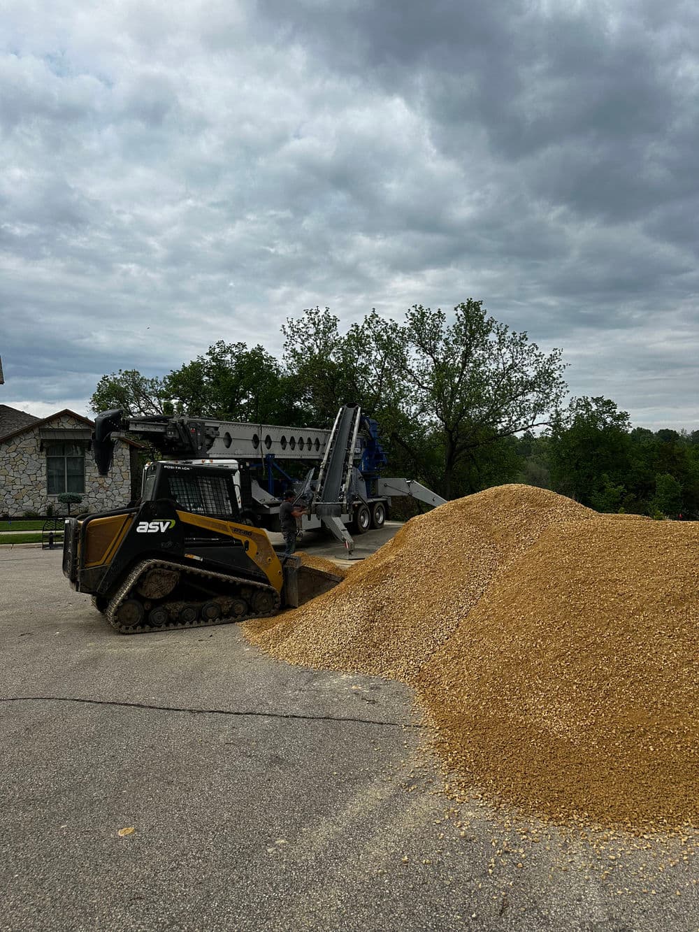 ASV mini skid steer loader moving gravel from a large pile on a cloudy day.