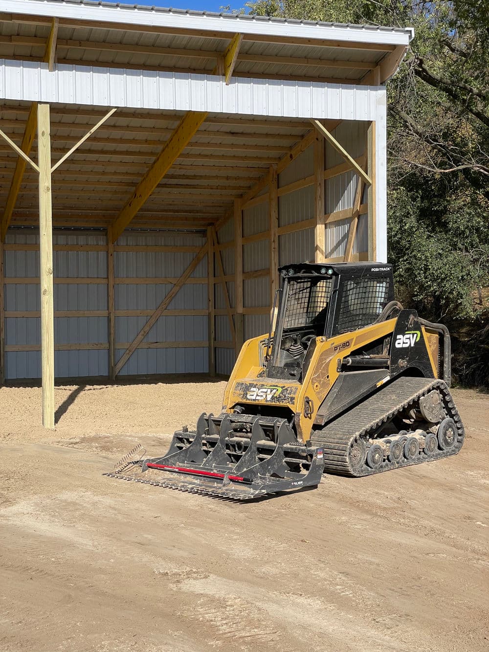 ASV skid steer loader parked inside a spacious barn with a dirt floor and wooden beams.