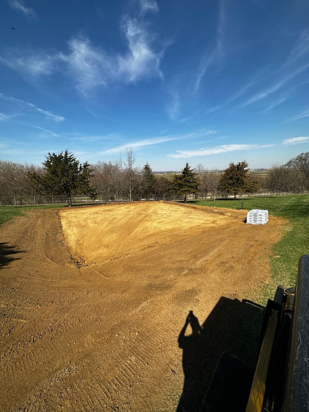 Cleared dirt site for construction with blue sky and trees in the background.